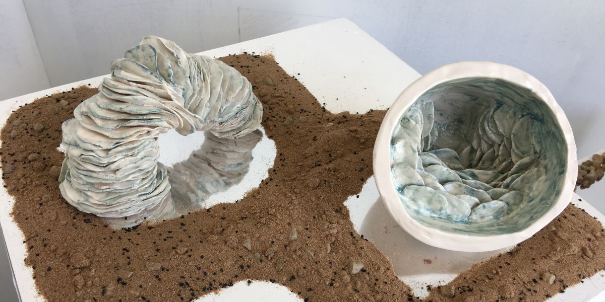 Glasgow Clyde College Art and Design student work. Pale blue clay piece surrounded by sand piece at exhibition.