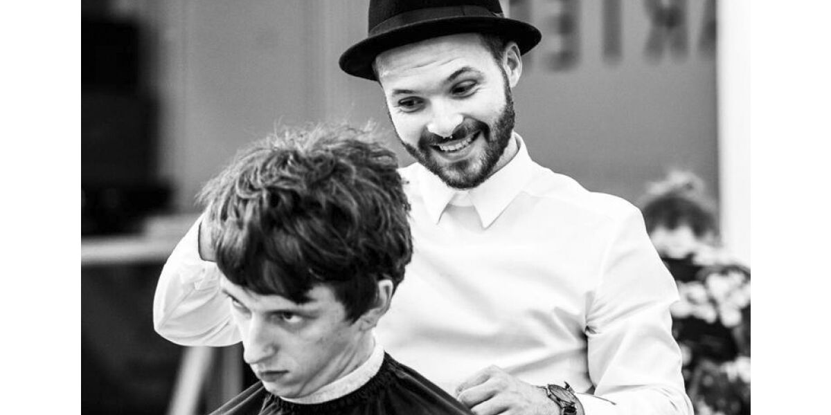 A man wearing a hat styling another man's hair in a hair salon.