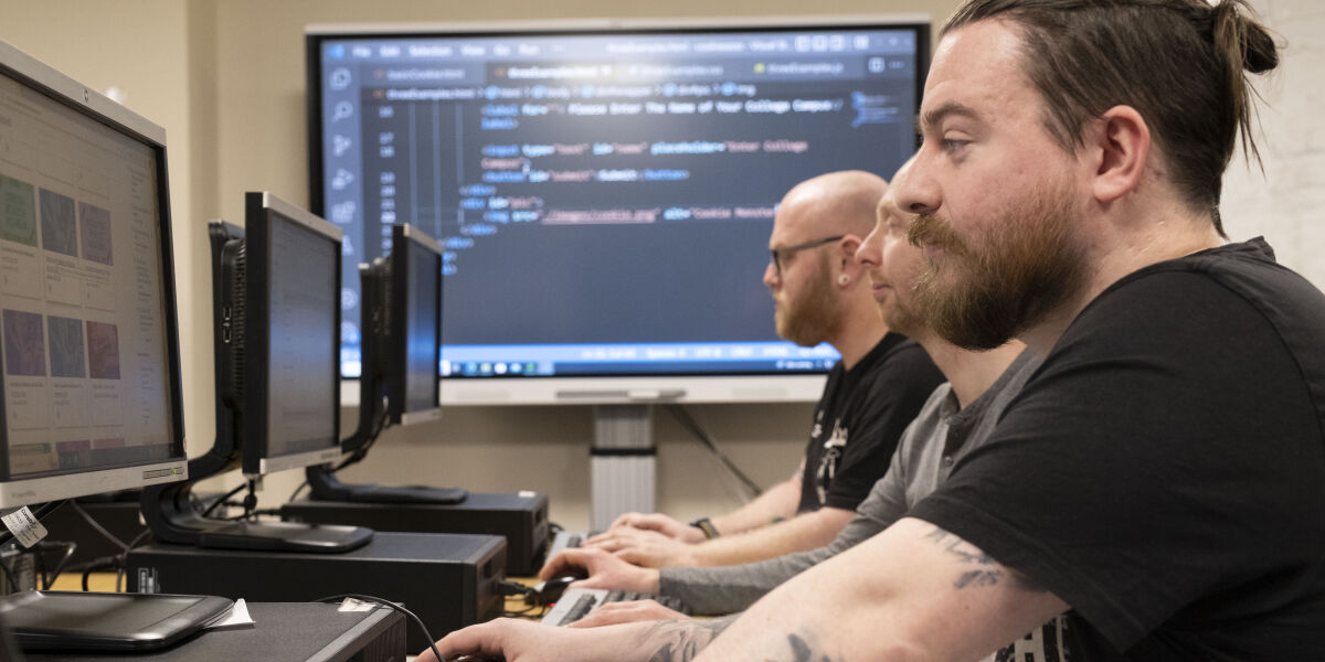 Male students learning to code on computers in class 