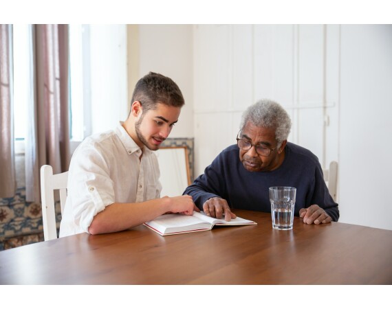 Image shows male student reading with elderly patient 