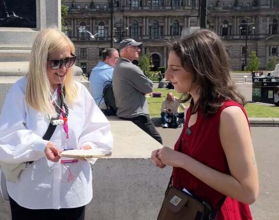 Image shows lecturer demonstrating embroidery technique to a lady in George Square.