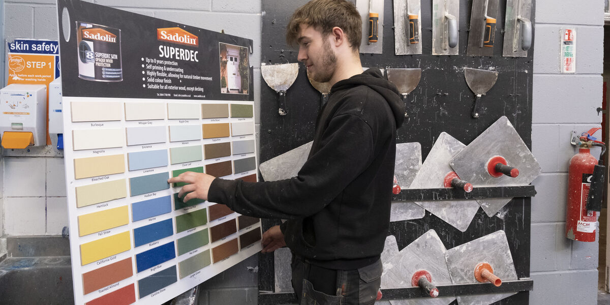 Male student choosing a paint colour surrounded by painting and decorating supplies