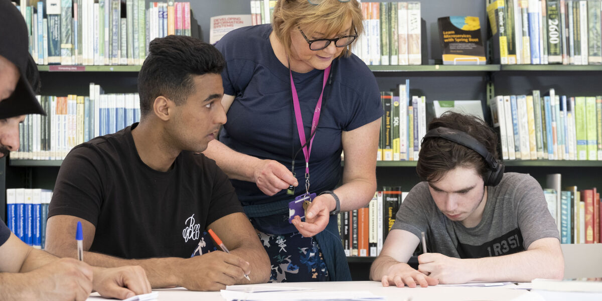 A lecturer supporting two students who are studying in the library. 