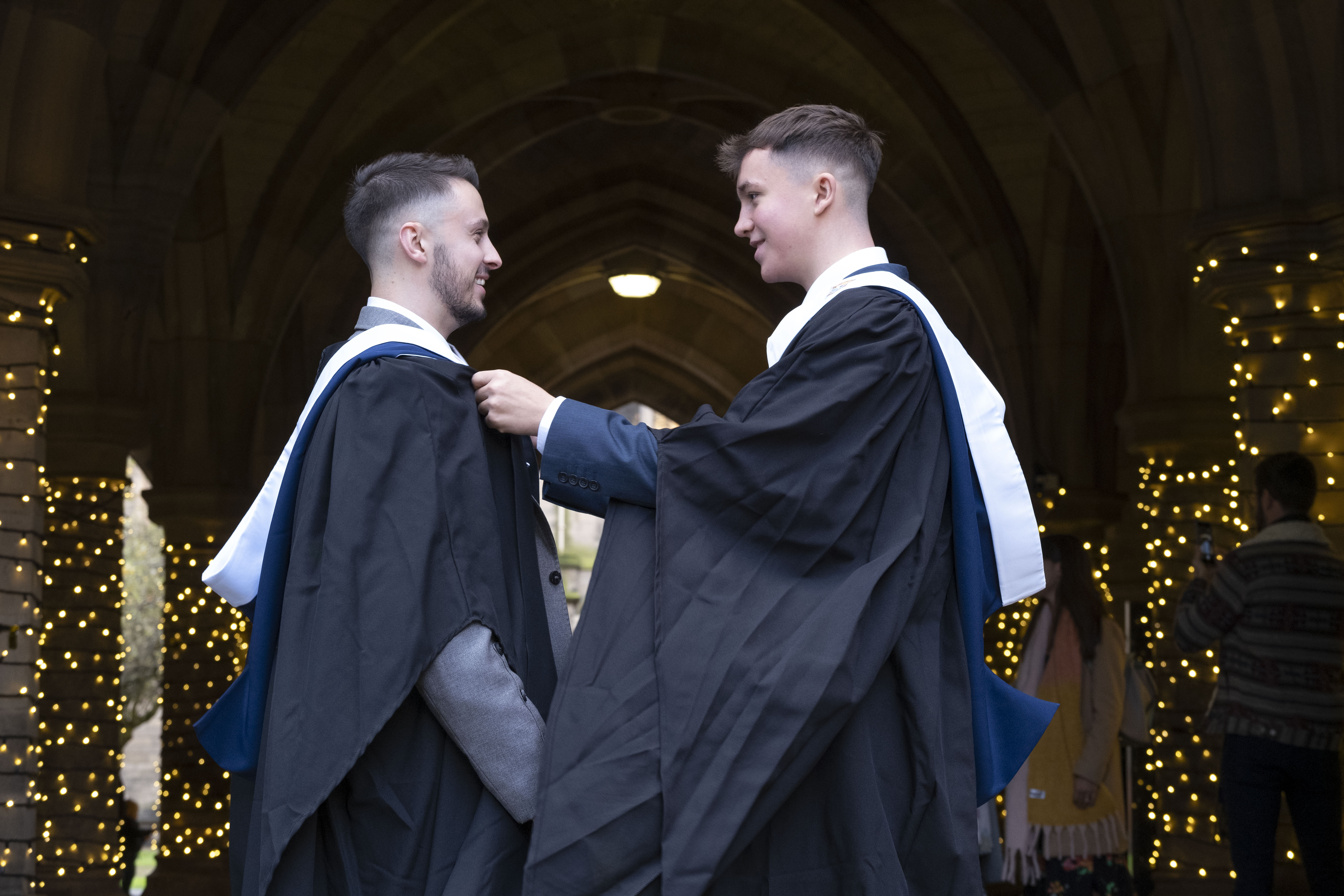 Two male graduates standing in cloisters