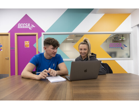 Two students sitting at a table looking at a laptop