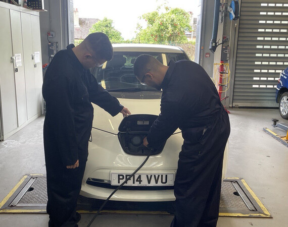 Two male automotive students working with electric vehicle charging point