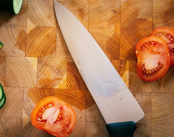 A wooden chopping board with a knife, some tomatoes and some cucumber on it. 