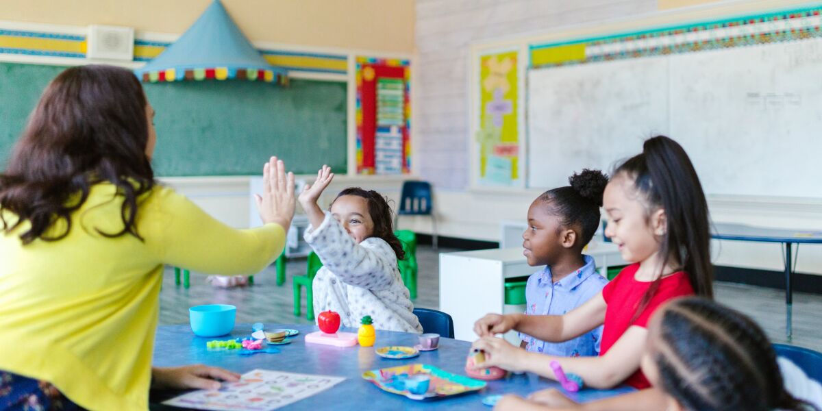 A group of children in a classroom doing a learning activity with a classroom assistant.