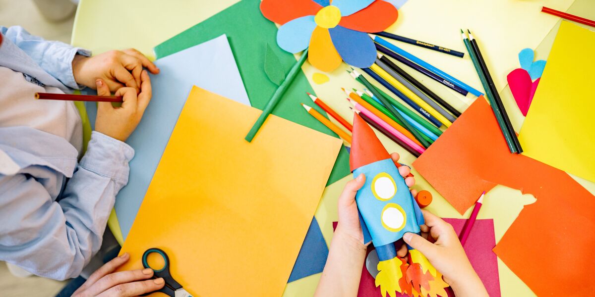 A table covered in colourful paper, pencils and scissors as children produce arts and crafts.