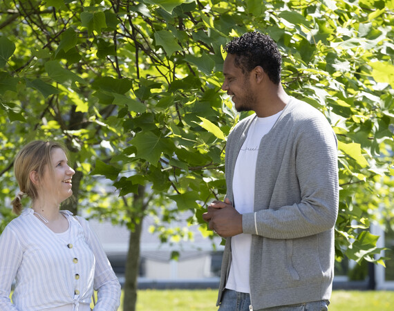 Female and male students chatting outside by a tree