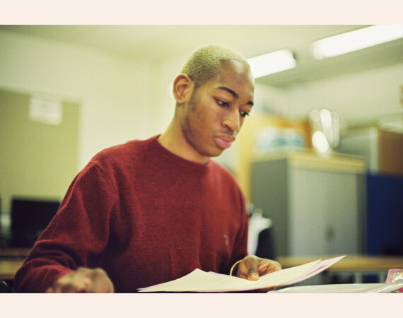 Image shows male student in classroom looking at workbook