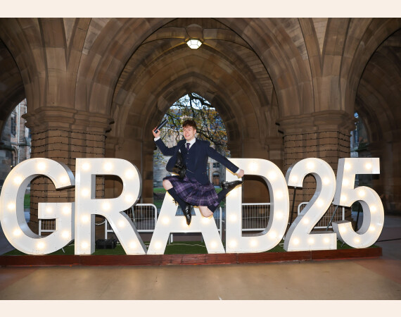 Image shows Ross Hoey leaping in front of lit up Grad 25 sign