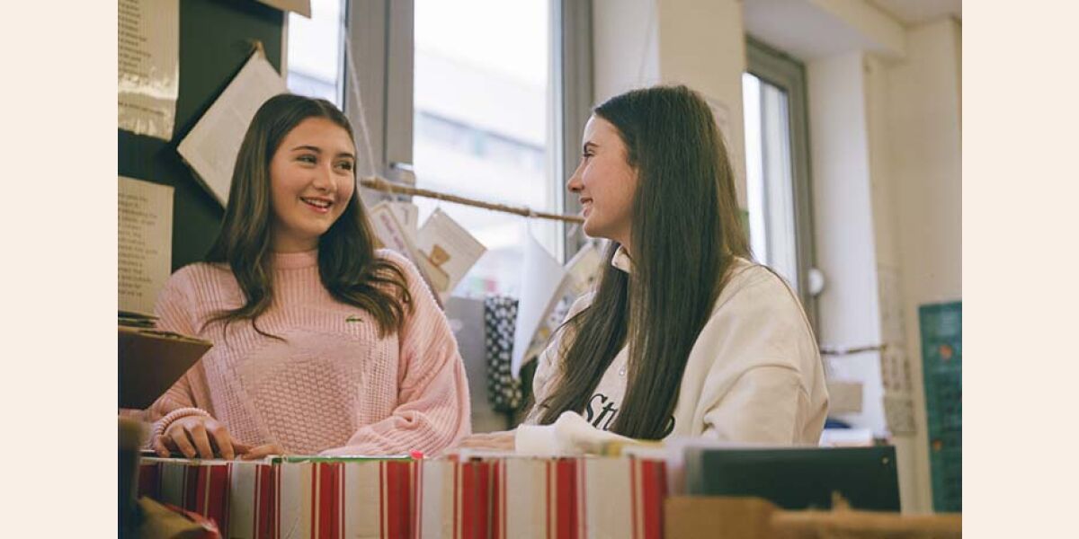 Two female students smiling and chatting in childcare classroom