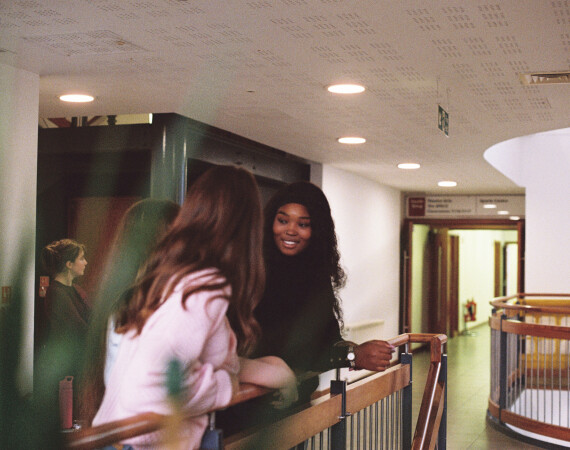 Two females chatting looking over Langside Campus foyer.