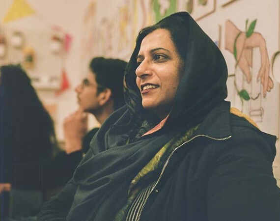 Female student wearing headscarf in classroom with other students in background.