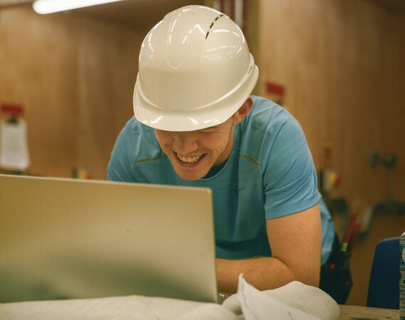 Construction student wearing a hard hat using a laptop. 