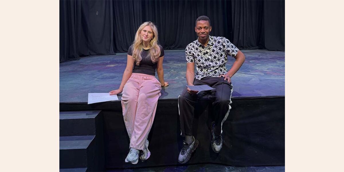 Image shows a female and a male senior phase acting student sitting next to each other on the stage at the Langside Campus theatre.