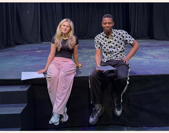 Image shows a female and a male senior phase acting student sitting next to each other on the stage at the Langside Campus theatre.